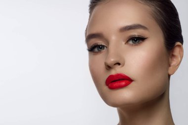 Klasik bir akşam makyajı ile kadın yüzünün güzelliğinin yakın çekim. Göz kapaklarında, uzun kirpiklerde ve kırmızı dudaklarda pürüzsüz siyah oklar. Güzellik ve kozmetoloji. Temiz yüz cilt