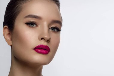 Klasik bir akşam makyajı ile kadın yüzünün güzelliğinin yakın çekim. Göz kapaklarında, uzun kirpiklerde ve pembe dudaklarda pürüzsüz siyah oklar. Güzellik ve kozmetoloji. Temiz yüz cilt