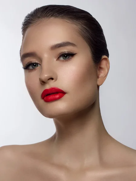 Close-up of the beauty of the female face with a classic evening make-up. Smooth black arrows on the eyelids, long eyelashes and red lips. Beauty and cosmetology. Clean face skin
