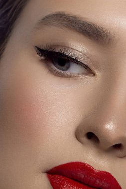 Yaratıcı moda gecesi makyajlı, yarı kadın yüzünün yakın plan güzelliği. Gözlerde siyah oklar ve son derece uzun kirpiklerde, dolgun dudaklarda kırmızı dudak rengi. Kaplıcadan sonra iyi bakımlı cilt