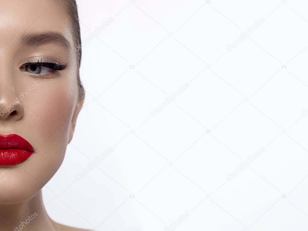 Close-up beauty of a half female face with creative fashion evening make-up. Black arrows on the eyes and extremely long eyelashes, on plump lips matte scarlet lip color. Well-groomed skin after spa
