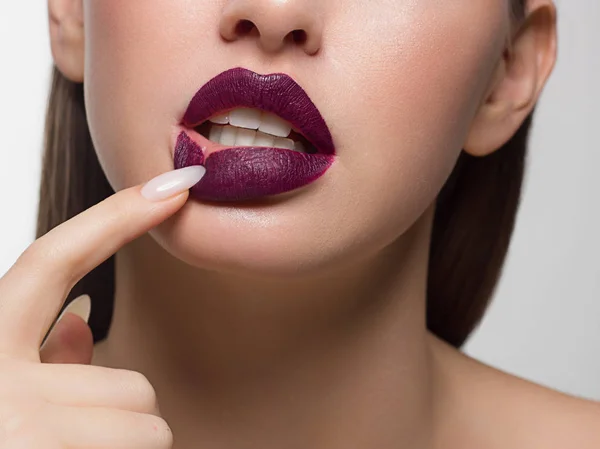 Close-up portrait of the lower half of a woman's face with sexy plump puple lips. Long nails pulling down the bottom lip. Rich lipstick and white teeth — Stock Photo, Image