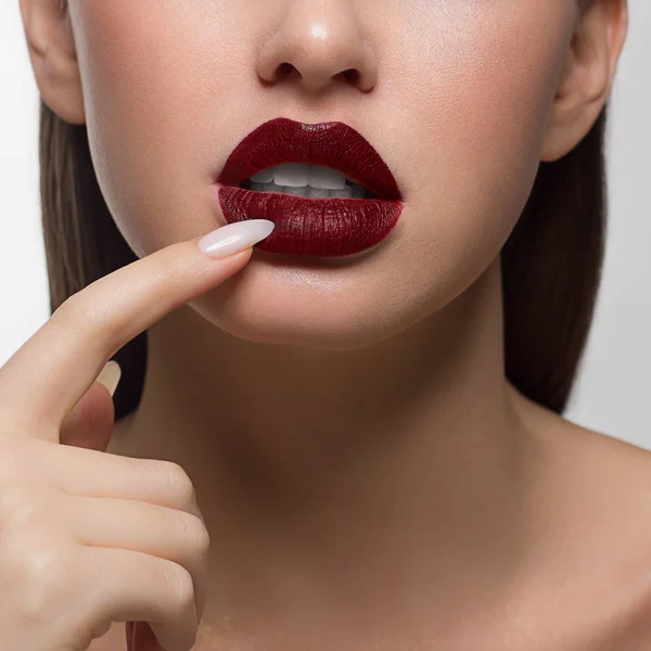 Close-up portret van de onderste helft van het gezicht van een vrouw met sexy mollige rode lippen. Lange nagels naar beneden trekken de onderste lip. Rijke lippenstift en witte tanden — Stockfoto