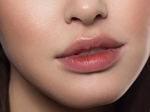 Καλλυντικά, μακιγιάζ και τάσεις. Λαμπερό lip gloss και κραγιόν στα χείλη. Κοντινό πλάνο του όμορφου γυναικείου στόματος με φυσικό μακιγιάζ χειλιών. Όμορφο μέρος του γυναικείου προσώπου. Τέλειο καθαρό δέρμα σε κόκκινο φως — Φωτογραφία Αρχείου