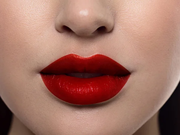 Καλλυντικά, μακιγιάζ και τάσεις. Λαμπερό lip gloss και κραγιόν στα χείλη. Κοντινό πλάνο του όμορφου γυναικείου στόματος με κόκκινο μακιγιάζ χειλιών. Όμορφο μέρος του γυναικείου προσώπου. Τέλειο καθαρό δέρμα σε κόκκινο φως — Φωτογραφία Αρχείου