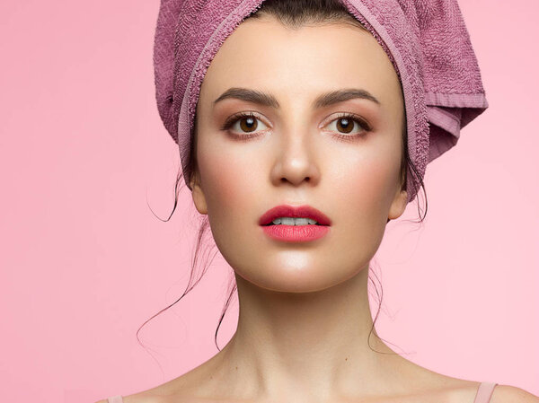 Beauty close-up with day makeup. Clean radiant skin of the face, a towel on his head. Spa treatments and beauty care. Beautiful eyes and white teeth. Pink background