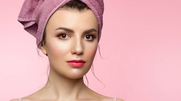 Beauty Woman face with hands. Beautiful Portrait Spa model Girl with Perfect Fresh Clean Skin. Female looking at camera and smiling. Youth and Skin Care Concept. Pink towel on the head, space for text