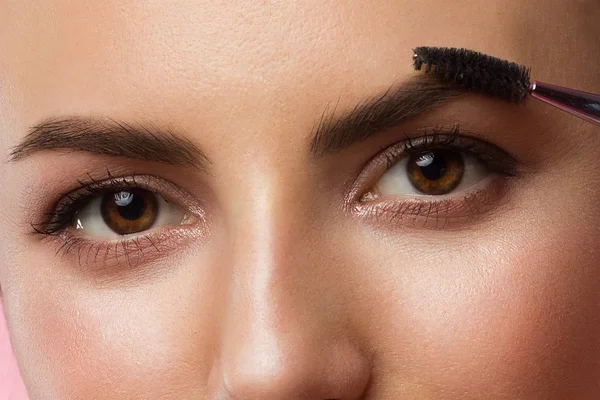 Nahaufnahme schöner Frauenaugen mit extrem langen Wimpern und klarer Haut. Mädchen kämmt Augenbrauen mit Augenbrauenbürste. Charmanter Blick in die Kamera — Stockfoto