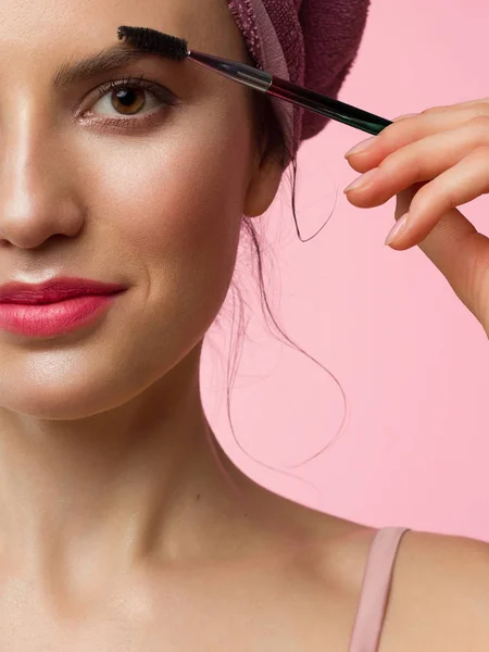 Female Slavic portrait of a young girl with brown eyes and light brown eyebrows close-up photo of half the face doing make-up eyelashes with mascara, natural beauty. Woman with a towel on her head