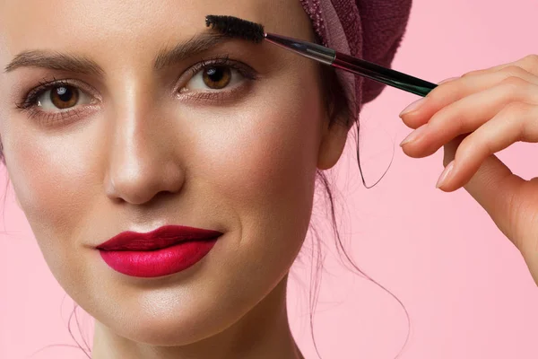 Primo piano di una bella donna con trucco naturale e pelle pulita con un asciugamano in testa. Le labbra paffute rosa. Ragazza pettinando le sopracciglia spesse e guardando la fotocamera. Cosmetologia e spa — Foto Stock