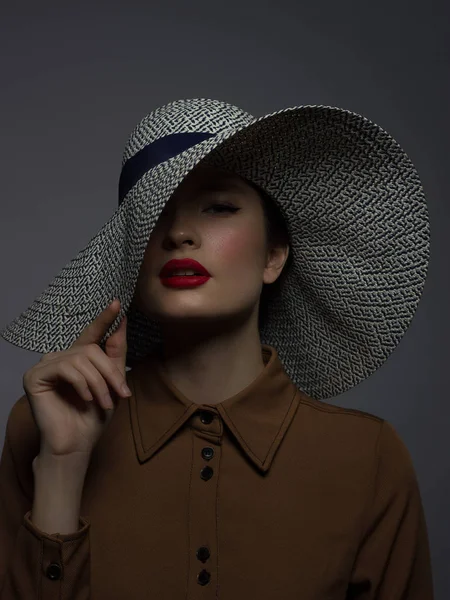 Beautiful woman portrait with red lipstick on lips and a big hat. Vintage image of a mysterious girl. Fashionable makeup. The hat covers half the face. Black eyeliner and extremely long eyelashes