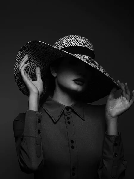 Beautiful woman portrait with red lipstick on lips and a big hat. Vintage look. Fashion makeup. The hat covers half the face. Black eyeliner and extremely long eyelashes. Black and white photography