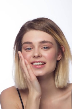 Güzel genç bir kadının temiz cildine ve kameraya gülümseyen saçlarına yakın çekim. Mavi gözlü bir sarışın portresi. Spa, cilt bakımı ve sağlık. Beyaz arkaplanda izole