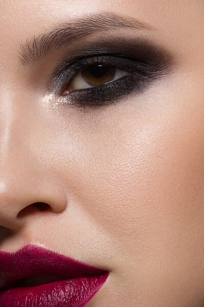 Close-up of the beauty of a woman's face with evening make-up emphasizing her expressive facial features. Smoky eyes, marsala-colored lips and clear skin. On an isolated black background