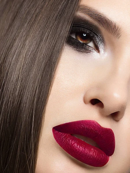 Beauty close-up van een vrouwelijk gezicht met een schone huid en sexy gelaatstrekken. Bruine ogen met rokerige zwarte schaduwen en highlighter. Mooie gladde wenkbrauwen en volle lippen de kleur van Marsala. Schone huid. — Stockfoto