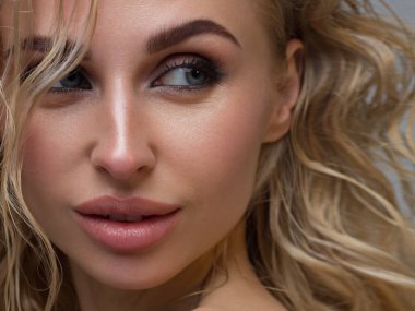 Siyah dumanlı göz makyajı ve doğal dolgun dudakları olan güzel bir kadının temiz yüzünün yakın plan portresi. Temiz ciltli, temiz yüzlü, uzun kıvırcık saçlı seksi bir manken. göz kamaştırıcı görüntü