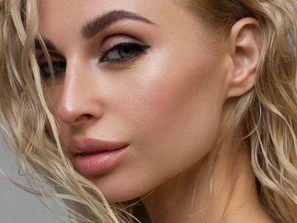 Beautiful woman with bright make up eye with sexy black liner makeup. Fashion big arrow shape on woman's eyelid. Natural lips. Chic evening make-up. Blonde long wave hair. Shining face skin