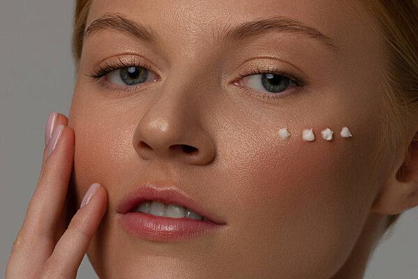 Young red-hair girl removing makeup from her face. Photo of beautiful girl with cotton pads on white background. Skin care and beauty concept. Copy space