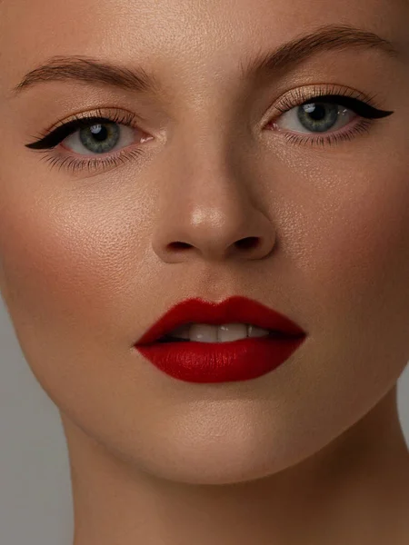 Close-up beauty of a female face with fashion evening make-up. Black liner on the eyes and extremely long eyelashes, on full lips matte scarlet lip color. Well-groomed skin after spa. red lipstick