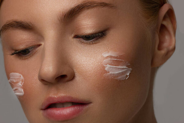 Skin care lady putting face cream. Attractive red-hair girl on white background. Beautiful face of young woman with cosmetic cream on a cheek. Skin care concept. Skincare products