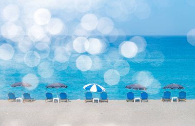 Güneş şemsiyeli ve güneşli yataklı yaz plajı. Güneşli sahil manzaralı beyaz bulutlu ve mavi güneşli yataklı. Yaz mevsiminde, ılık güneş ve beyaz bokeh ışıklarıyla bomboş deniz kıyısında.