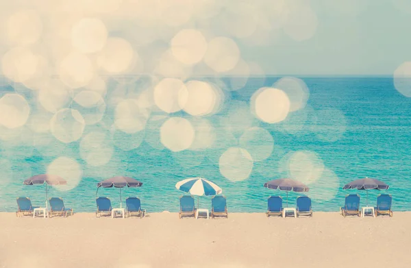 Güneş şemsiyeli ve güneşli yataklı Retro Ummer Plajı. Manzaralı beyaz bulutlu güneşli sahil ve klasik tonlarda mavi güneşli yatak. Yaz mevsiminde, ılık güneş ve beyaz bokeh ışıklarıyla bomboş deniz kıyısında.