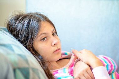 Genç kız yatakta yatıp sıcaklığı kontrol ediyor.