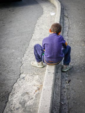 Mor kazak ve kot Genç çocuk sokak kenarlığın üzerine oturur ve geleceğini düşünmek