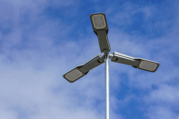 Three LED street lamps affixed to an iron post against a deep blue sky