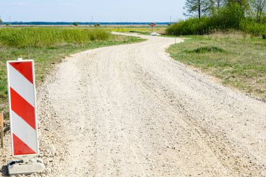 Kırsal kesimde dolambaçlı yol, ön planda uyarı işareti