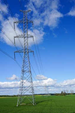 high-voltage power transmission line in a cereal field on a background of blue sky with white clouds clipart
