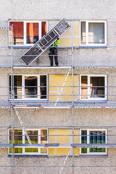 an employee in safety equipment assembles scaffolding on the facade of a multi-storey house at a dangerous height