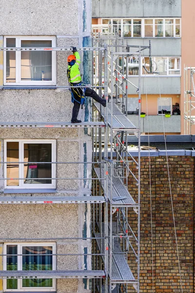 an employee in safety equipment assembles scaffolding on the facade of a multi-storey house at a dangerous height