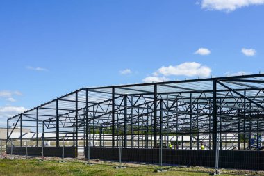 Yeni bir modern sanayi binasının inşası, mavi gökyüzünün arka planında metal kiriş iskeleti.
