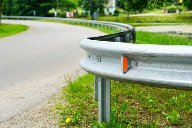 Önünde metal koruma bariyeri olan asfalt yol kıvrımlı.