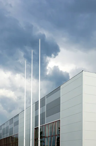 new building sandwich panel facade and three flagpoles without flags on a background of gray storm clouds