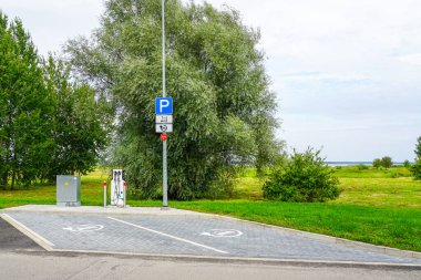 Yeşil bir açık hava ortamında belirlenmiş park yerleri olan modern EV şarj istasyonu, sürdürülebilir ulaşımı teşvik ediyor