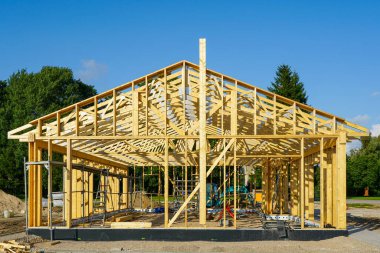 Güneşli bir günde çatı kirişleri, kirişleri ve iskelesi olan ahşap bir evin önü.