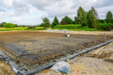 İnşaat alanına beton temel döşeme için takviye çelik ağ şebekesi kurulmuş, inşaat malzemeleri görünür.