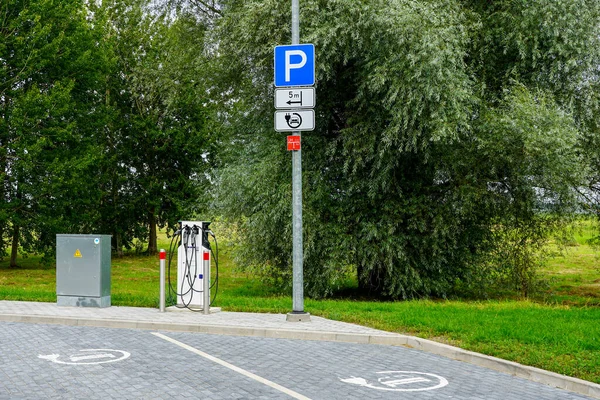Kamu elektrikli araba şarj istasyonu, kablolar, park işaretleri ve yeşil yol kenarındaki park alanında elektrik ünitesi.