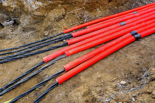 Kalın siyah elektrik kabloları kırmızı kıvrımlı koruyucu kanallara bağlanıyor. Bir tesis tesisinin toprak siper zeminine yerleştirilmiş.