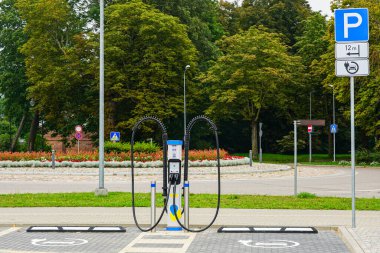 İkili şarj kablolarıyla kamu elektrikli araba şarj istasyonu, işaretli EV park noktaları ve şehir ortamında trafik işaretleri