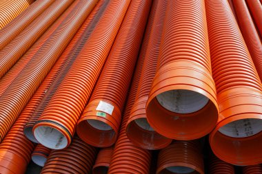 Büyük turuncu kıvrımlı plastik borular inşaat için istiflenmiş, genellikle drenaj ve kanalizasyon sistemlerinde uygulanır.