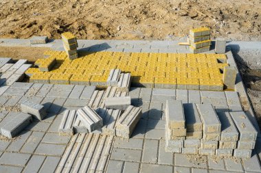 Sarı ve gri beton kiremitlerle dokunsal asfalt döşeme kurulumuna yakın çekim, görme engelli yayalar için güvenli navigasyon sağlar