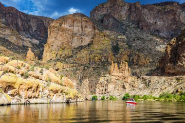 One red and white boat on the calm waters of Canyon Lake in Arizona surrounded by cliffs from the tall rock Superstition Mountains in the Tonto National Forest clipart