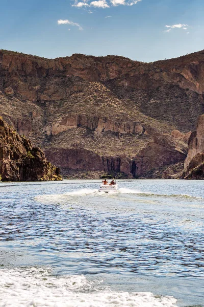 People on boat driving into canyon on lake in Arizona surrounded by mountains on a hot summer day