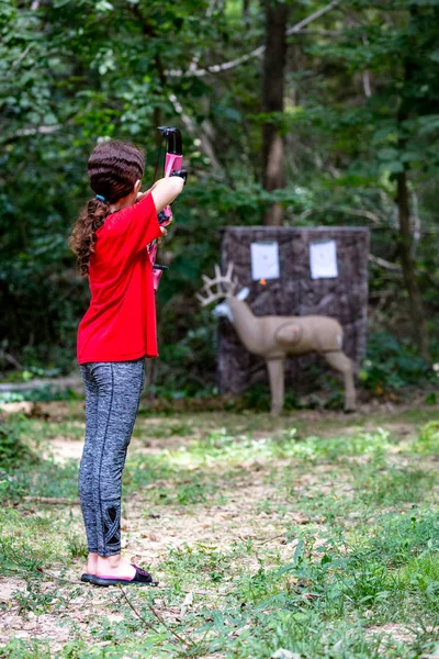 Pre-teen girl using bow and arrow to practice deer hunting archery skills on model target in the woods
