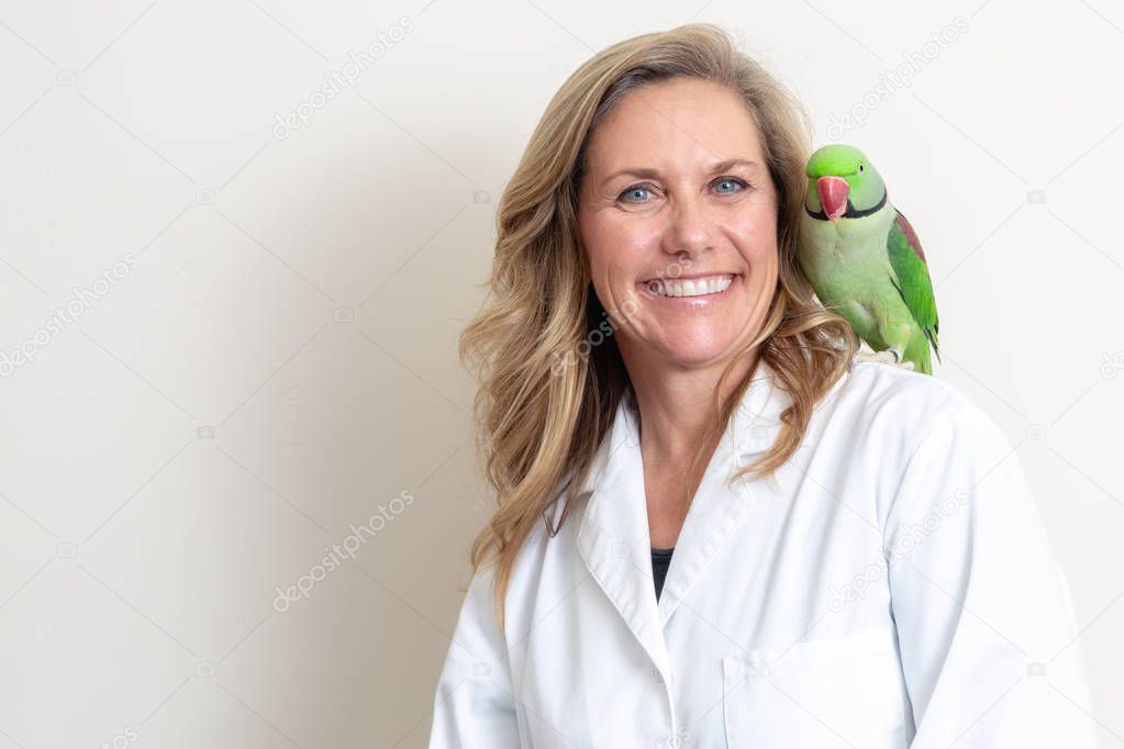 Happy and friendly female veterinarian with a green Alexandrine parrot bird on her shoulder