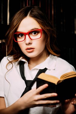 Güzel kız giyiyor okul üniforma eski kütüphanede onu elinde bir kitapla duruyor. Güzellik, moda. Eğitim kavramı.