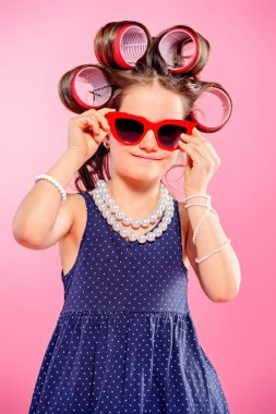 Güzel bir kız ile güneş gözlüğü saçında curlers portresi. Stüdyo pembe arka plan üzerinde vurdu. Çocuk moda. 